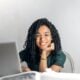 Woman smiling into the camera with laptop on table