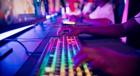 Diverse gamer group players playing competitive MOBA PvP top down view computer game on a stage. Close-up on the hands
